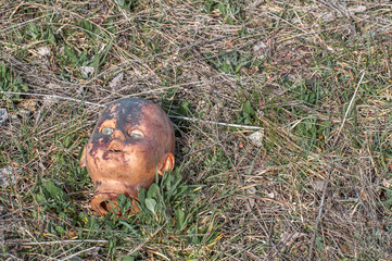 Creepy old doll head. Broken abandoned damaged scary toy in a garbage dump close-up. In the toy, the eye and mouth are damaged. The concept of fear, horror, crime. Very scary.