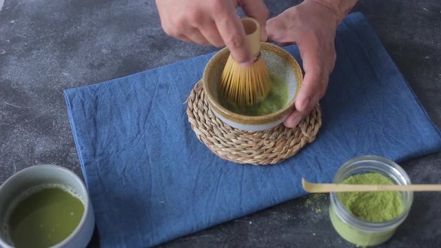 Man mixing green tea matcha in a bowl on blue surface. Drink is a rich source of antioxidants and polyphenols 