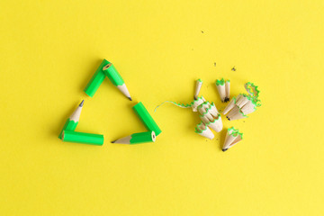 Flat lay of triangular eco recycle icon made of pencils with pencil scraps on yellow background minimal creative eco concept.