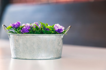 An artificial flower in metal bucket on white table.