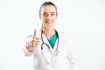 Young smiley nurse puts thumb up, wears scrub uniform and stethoscope.