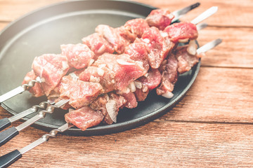 A number of skewers with meat laid out in a black plate. Close-up of mouth-watering pieces of beef ready to fry. Meat dish. Top view on wooden background