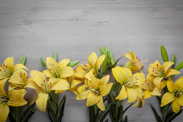 Bouquet of bright yellow lilies on a light wooden background.