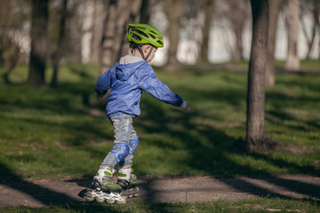 Cute boy in the park rides on the rollers. Sunny and warm.