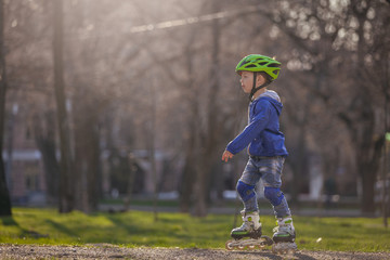 Cute boy in the park rides on the rollers. Sunny and warm.