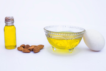 Best home remedy to repair hair damage isolated on white i.e. Egg white along with almond oil in a glass bowl with all the raw ingredients.