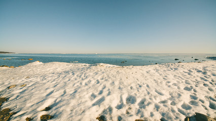 Snow pile on the beach, hill. Large snow drift isolated on a blue sky background,  outdoor view of ice blocks at frozen finland lake in winter