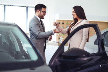 Saleswoman giving keys of new car to male client