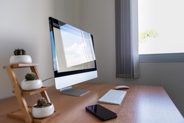 All-in-one computer with smart phone and cactus on wooden table near window