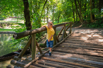 Naklejka na ściany i meble little boy walking near village lake on wooden bridge