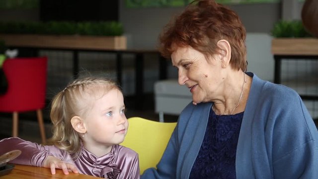 Grandmother tells a story to her granddaughter. An elderly retired woman tells stories to her little girl granddaughter in a cafe