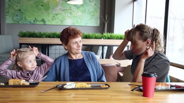 Mom tells a fairy tale to her granddaughter. A young woman tells stories to her little girl daughter to her mother to her grandmother in a cafe.
