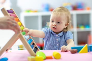 Little kid girl plays with abacus sitting at table