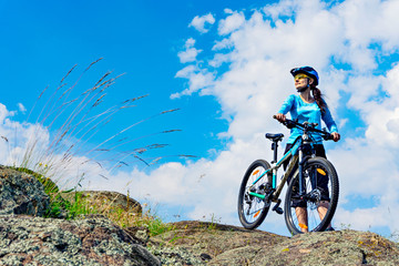 Woman cyclist stands on the hilltop with her mountain bike.