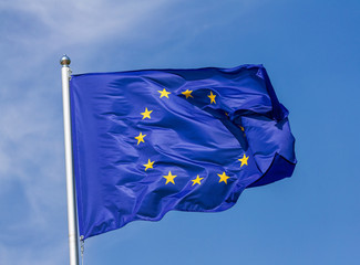 Flag of the European Union waving in the wind on flagpole against the sky with clouds on sunny day, close-up