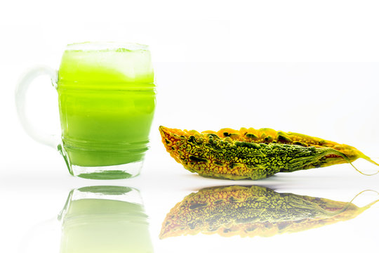 Raw organic bitter melon or bitter gourd with its extracted juice in a transparent glass with some ice cubes with reflection isolated on white.