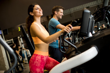 Young woman and man on elliptical stepper trainer exercising in gym