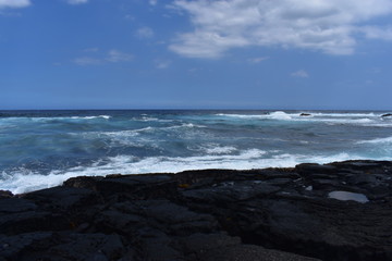 Waves Crashing on Rocky Shore in Hawaii white foam as the waves wash over the rocks under a blue sky