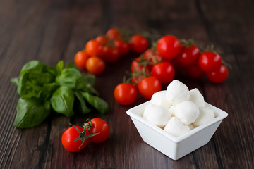 Mozzarella cheese, basil and cherry tomatoes on a brown wooden table. Ingredients for making salad caprese. Mediterranean Kitchen.