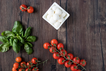 Mozzarella cheese, basil and cherry tomatoes on  brown wooden table. Ingredients for making salad caprese. Mediterranean Kitchen.