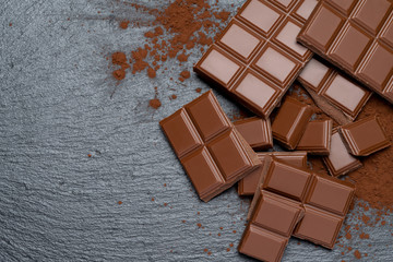 Dark or milk organic chocolate pieces and cocoa powder on dark concrete backgound