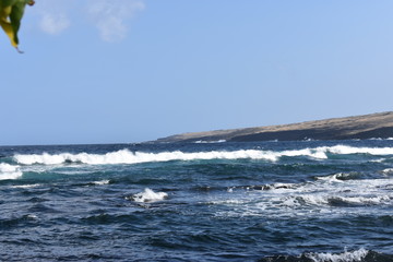 Waves Crashing on Rocky Shore in Hawaii white foam as the waves wash over the rocks under a blue sky