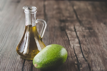Avocado oil in glass jug on  brown wooden background. Healthy food.