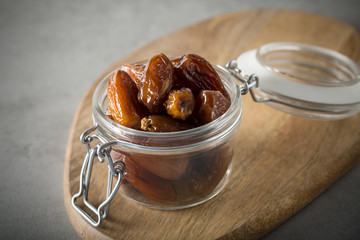 Dried dates in a glass jar on a light grey marble table.