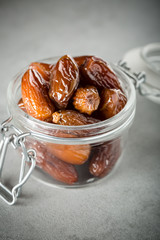 Dried dates in a glass jar on a light grey marble table.