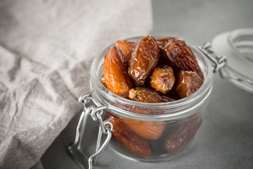 Dried dates in a glass jar on a light grey marble table.