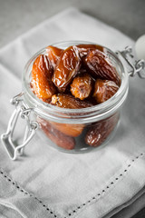 Dried dates in a glass jar on a light grey marble table.