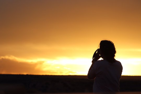 Woman in silhouette photographing the New Mexico sunset sky.