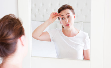 Middle age woman looking in mirror on face wrinkle forehead in bedroom. Wrinkles and anti aging skin care concept. Selective focus. Banner