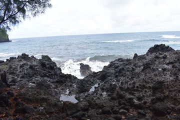 Waves Crashing on Rocky Shore in Hawaii white foam as the waves wash over the rocks under a blue sky