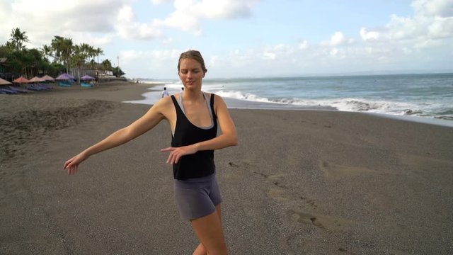 Young, fit woman stretching arms, exercising on the beach