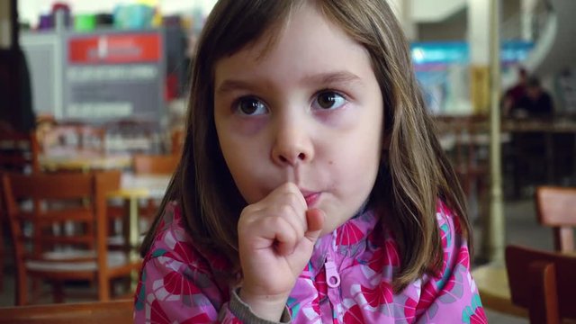 Eating and childhood concepts. A little girl, a child of 4-5 years old, eats chupa chups, sitting at a table on a food court.