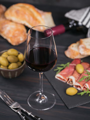 Glass of red wine with slices of cured ham or Spanish jamon serrano or Italian prosciutto crudo, bread, green olives and arugula