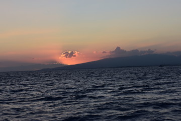 Bright sky at sunset over the Pacific Ocean in Hawaii Sun dipping behind mountain and cloud throwing all sorts of colors into the sky