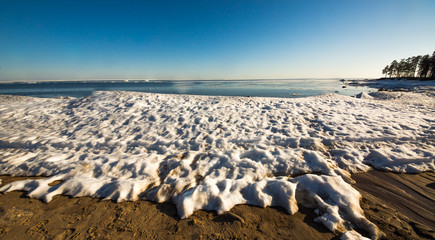 Snow pile on the beach, hill. Large snow drift isolated on a blue sky background,  outdoor view of ice blocks at frozen finland lake in winter