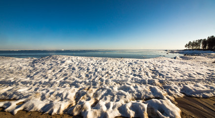 Snow pile on the beach, hill. Large snow drift isolated on a blue sky background,  outdoor view of...
