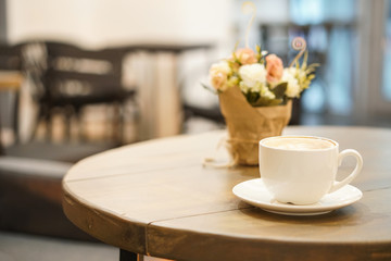 Cup of cappuccino on wooden table. Blurred background cafe behind.