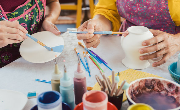 Woman coloring handmade dishes using brush and color