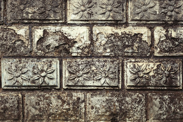 Stone wall with flower relief on each stone brick, old and weathered