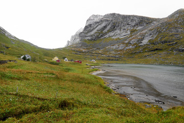 Fototapeta premium Panoramic view over a small village at the coastline with a beach and surrounding mountains on the way to Bunes Beach on Lofoten Islands in Norway.