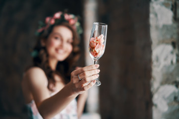 Beautiful woman holding wineglass with rose petals cheers to camera