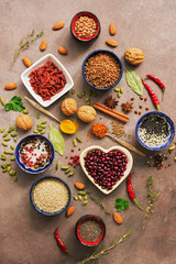 Super food background, a variety of cereals, legumes, spices, herbs, nuts. Various seasonings for cooking on brown background. Top view, overhead.