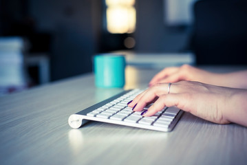 Obraz na płótnie Canvas Woman hands with polished nails typing on white wireless keyboard.