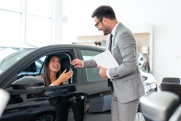 Professional salesman giving car keys to customer in car showroom.