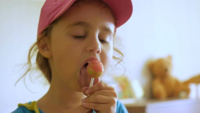 Little girl enjoying a lollipop while staring at camera. Child eating candy, sweets, sugar