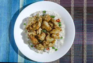 appetizing chicken in sweet and sour sauce and rice with vegetables and pepper on a white plate multicolor background top view